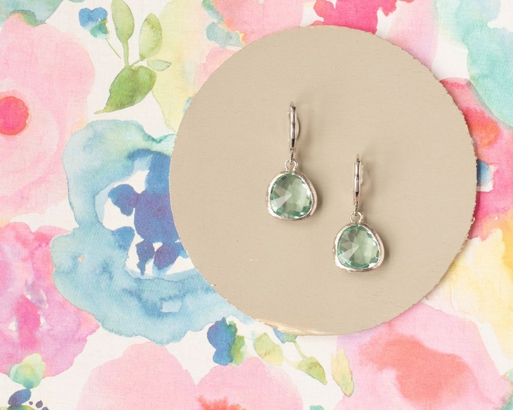 Green teardrop earrings on a beige circular card with a colorful floral background