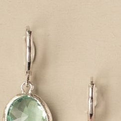 Green teardrop earrings on a beige circular card with a colorful floral background