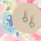 Green teardrop earrings on a beige circular card with a colorful floral background