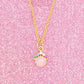 Gold necklace with a pink pendant on a pink glittery card