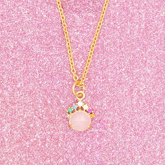 Gold necklace with a pink pendant on a pink glittery card
