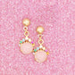 Gold earrings with pink gemstones on a pink glittery background