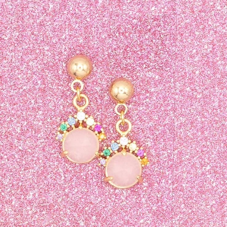Gold earrings with pink gemstones on a pink glittery background
