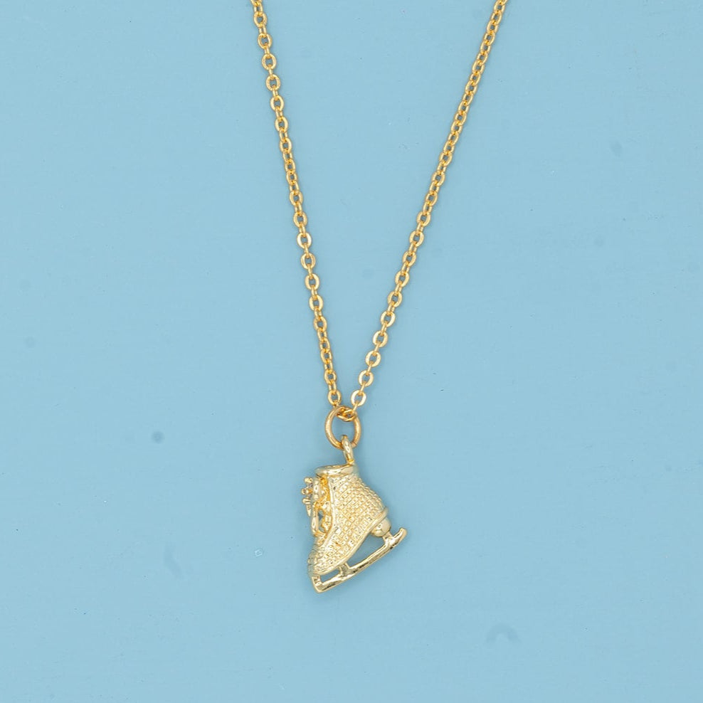 Gold ice skate pendant necklace on a blue card with a light blue background