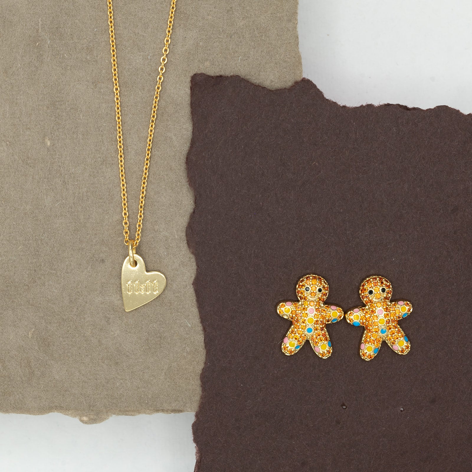 Gold necklace with a heart pendant and gingerbread man earrings on a textured surface.